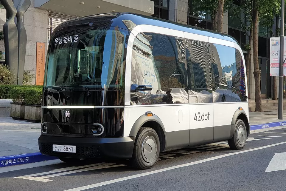 A small boxy driverless shuttle pulled up to a curb.